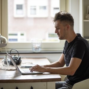 Young man focused on working from home on his laptop at a kitchen table.